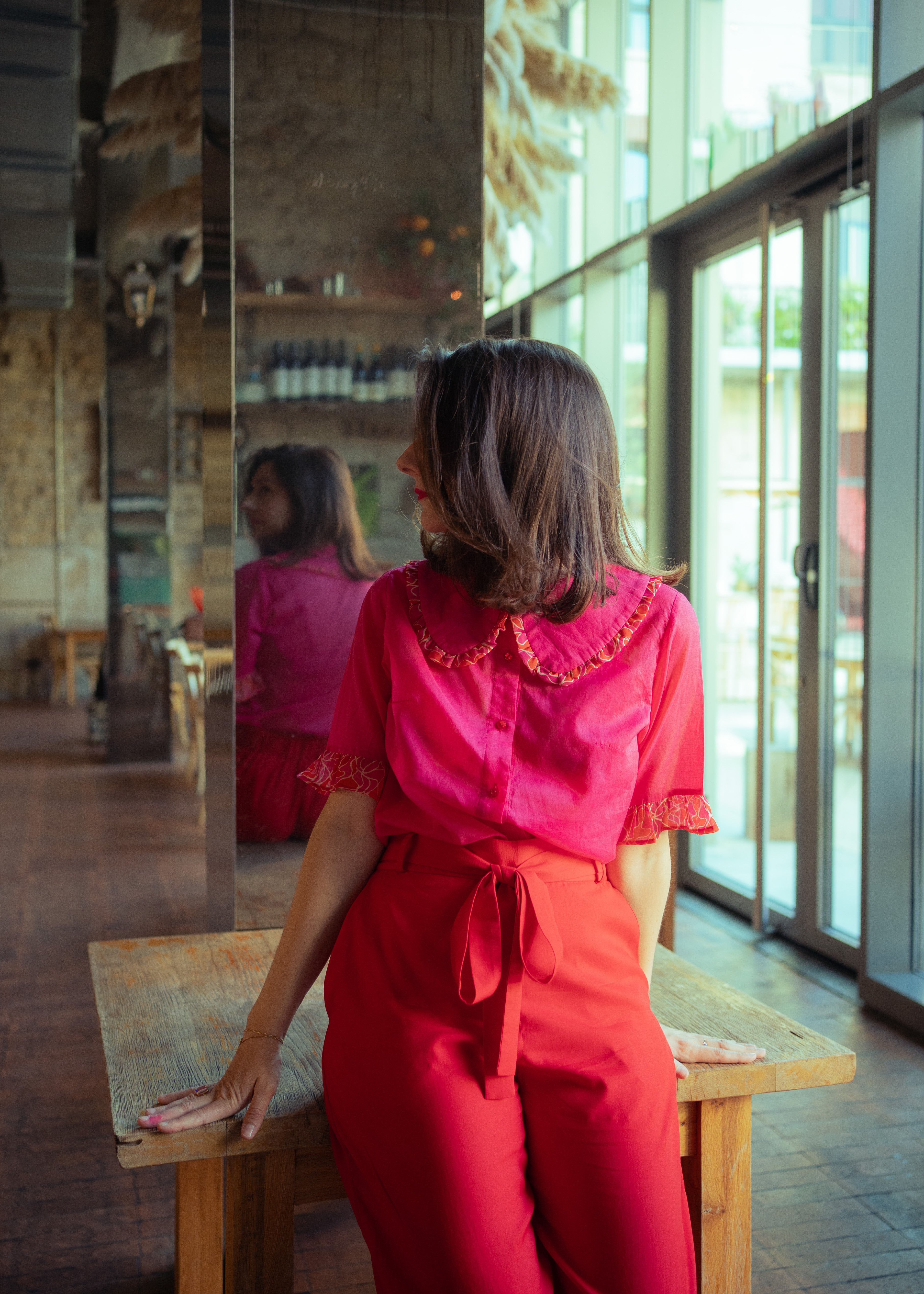 Photo de shooting mode de vêtements colorés : une chemise rose fuschia à maxi col claudine et aux motifs géométriques d'inspiration rétro, avec un pantalon rouge ceinturé taille haute.